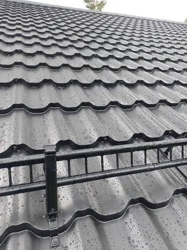 Copilot said: Nærbilde av mørkt metalltak med snøfanger og regndråper på takplatene etter nedbør.
