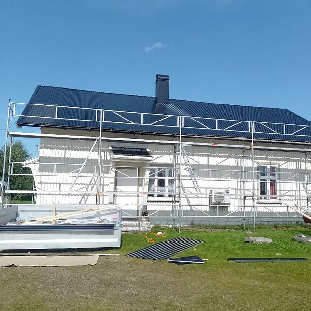 Hvit enebolig med nytt mørkt tak og stillas rundt fasaden under pågående takarbeid.