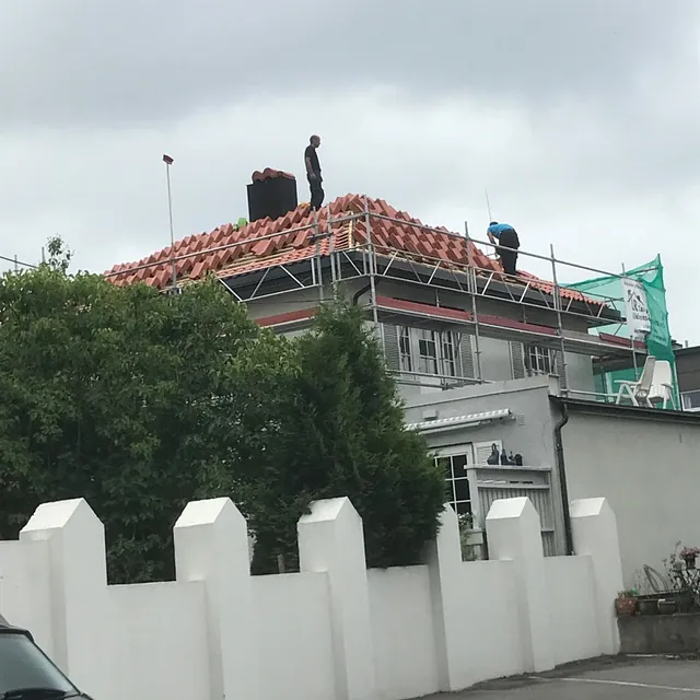Arbeidere legger takstein på boligtak fra stillas under takrenovering i overskyet vær.