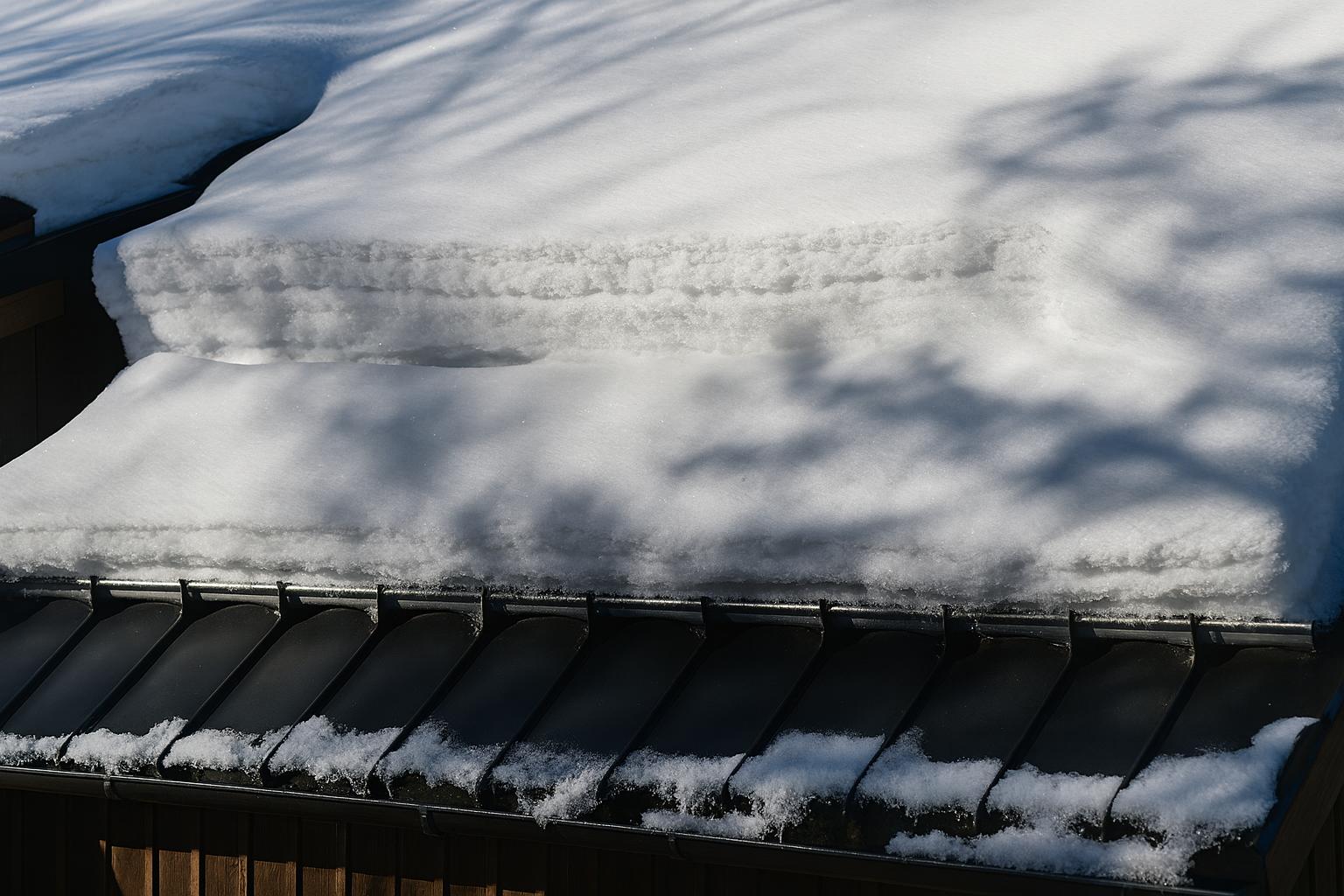 Snødekt tak med stort snølag og synlig takfot, fotografert i vinterlys med skyggespill.