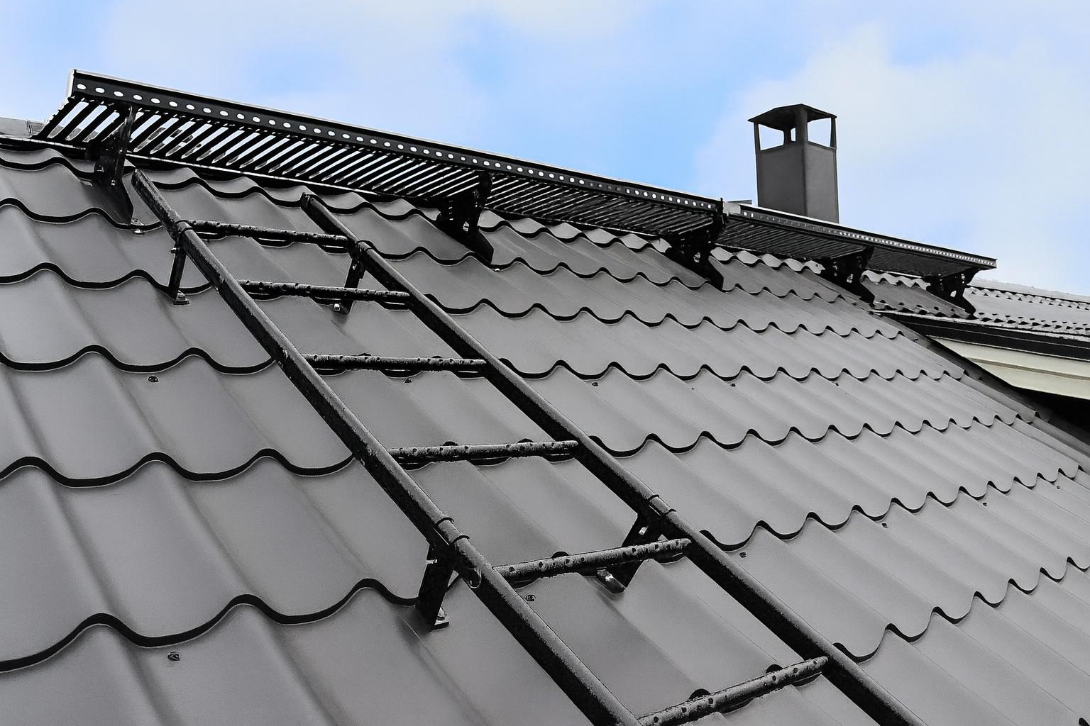 Tak med snøfangere, takstige og pipe montert på grått metalltak med taksteinsprofil.
