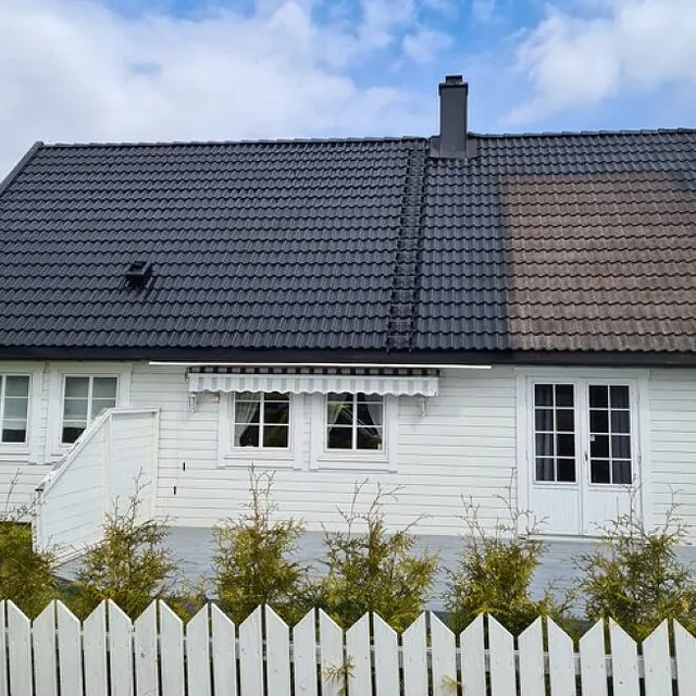 Hvit enebolig med mørkt tak, pipe og inngjerdet hage fotografert fra fremsiden.