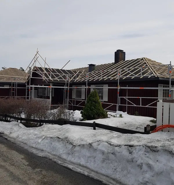 Enebolig under takrenovering med stillas, nye lekter og snødekt tomt i boligområde.