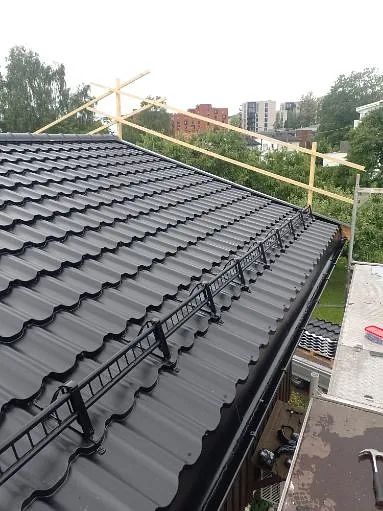 Mørkt metalltak med snøfangere og taksikringsutstyr montert langs takfoten på boligbygg.