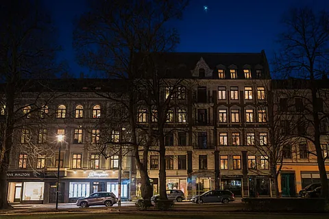 Bygårder med opplyste vinduer og butikklokaler langs gate i bymiljø fotografert om kvelden.